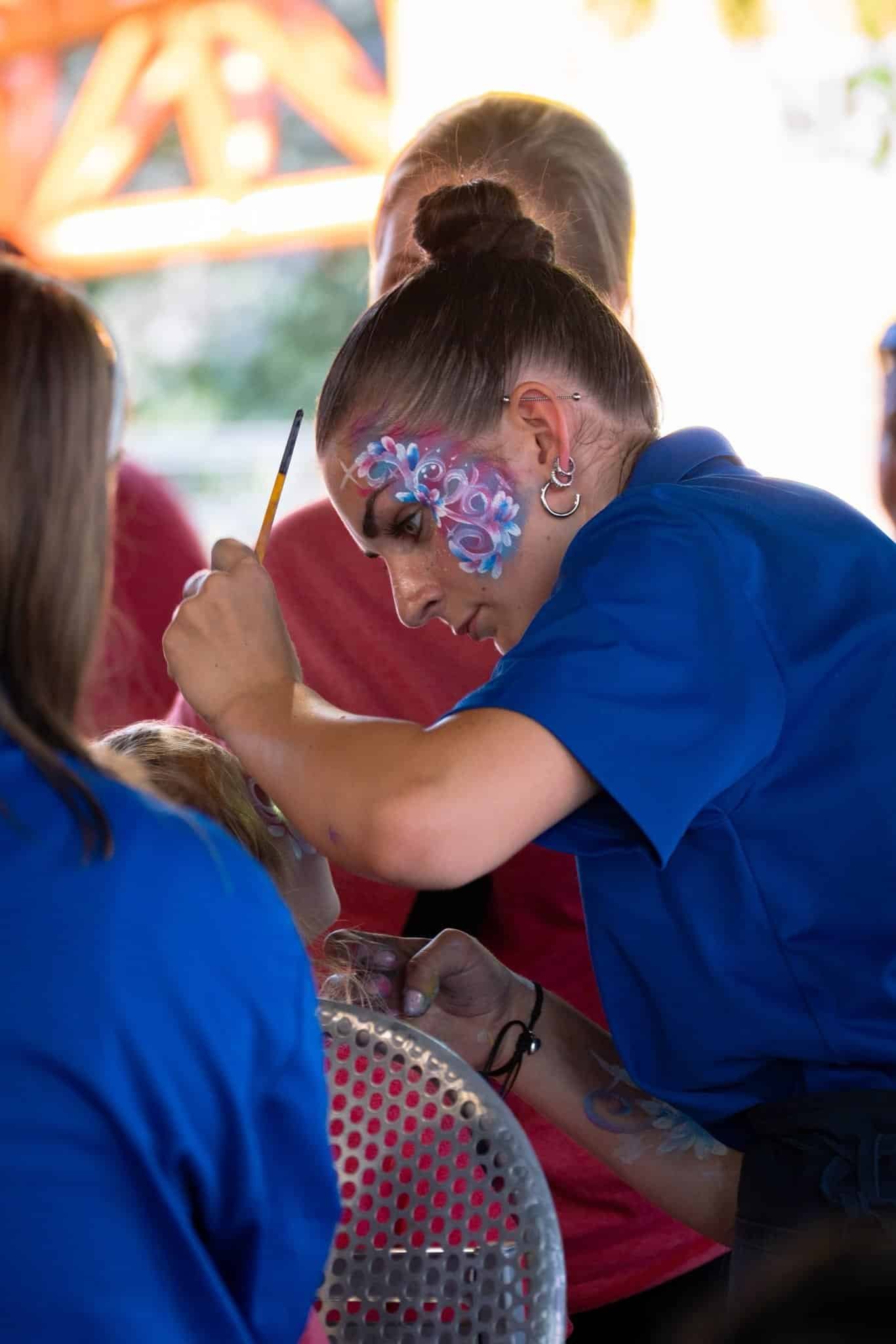 Photograph of a event worker doing face painting for children at a work retreat.