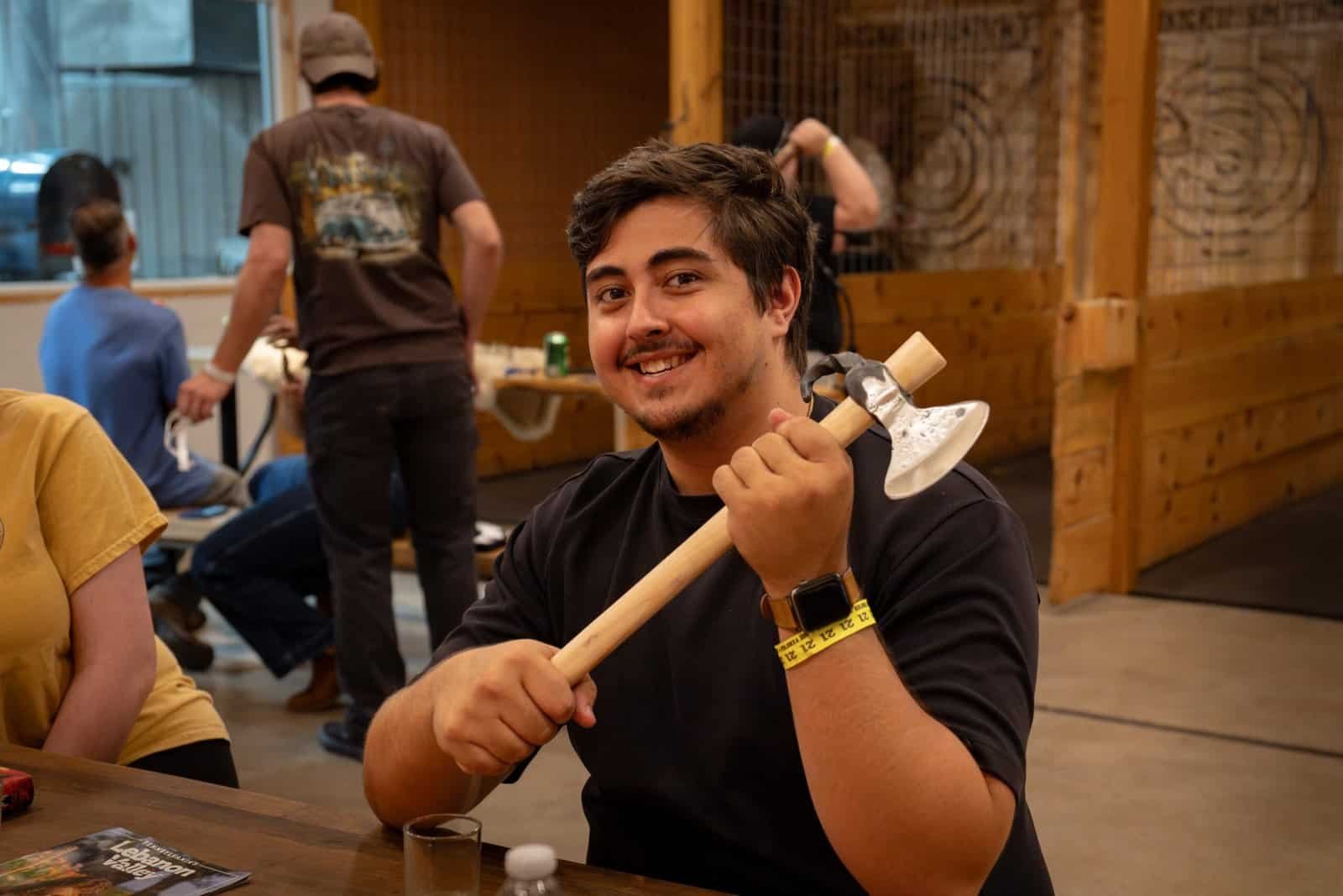 Photograph a man smiling holding a hatchet he build.